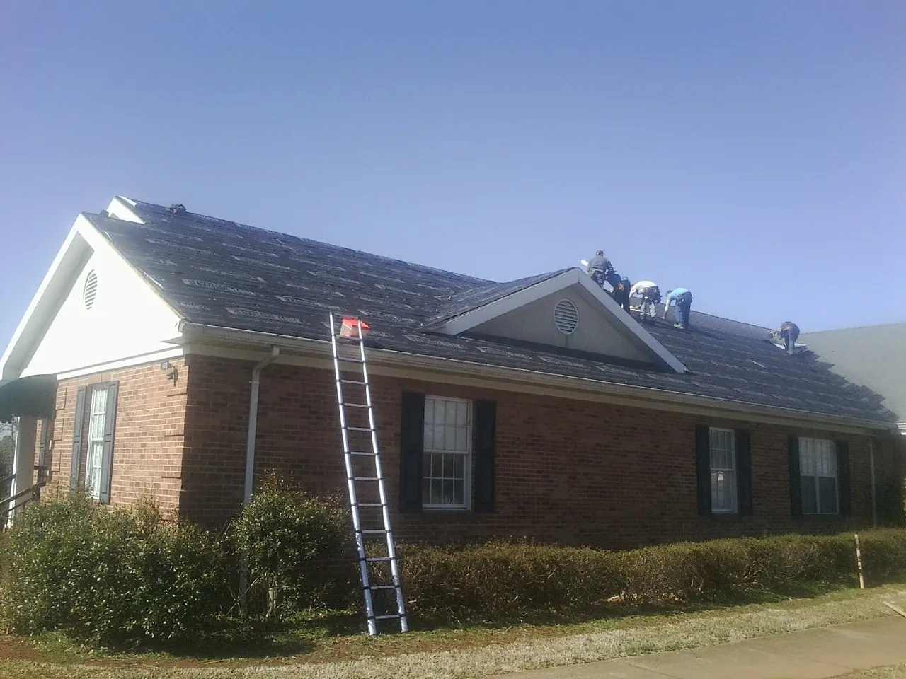 Crew tearing shingles off a brick ranch roof with a ladder set — Metal Roof Repair work by our crew in Hartleton