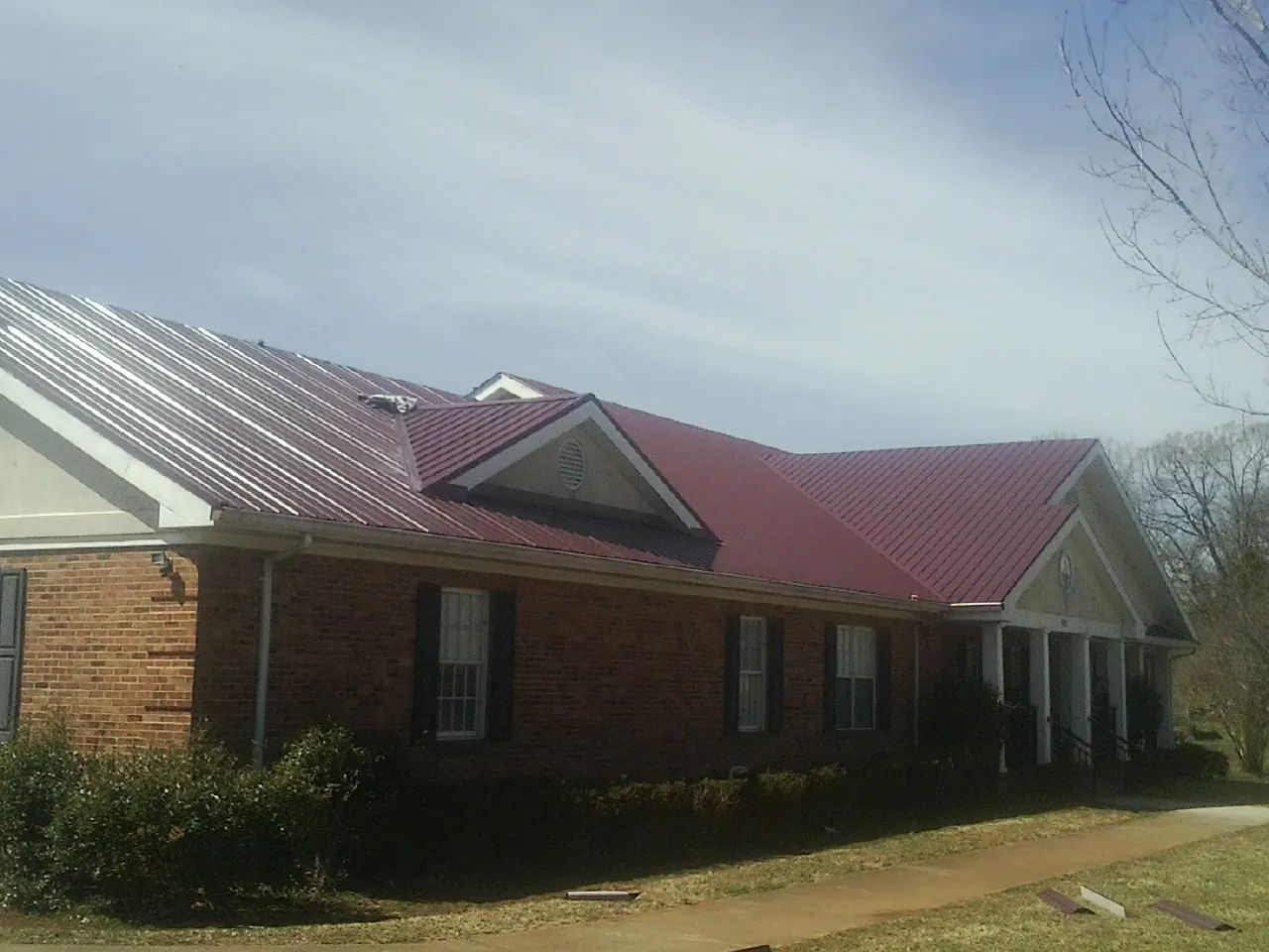 Red metal roof with gabled entries on a long brick building, from a Hail Damage Roof Repair job in Hartleton