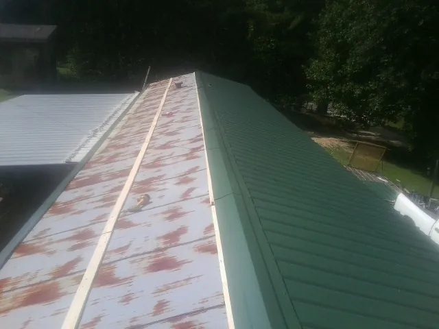 Old rusted panels beside newly installed green metal roofing — Wind Damage Roof Repair by Roofing Brothers in Hartleton