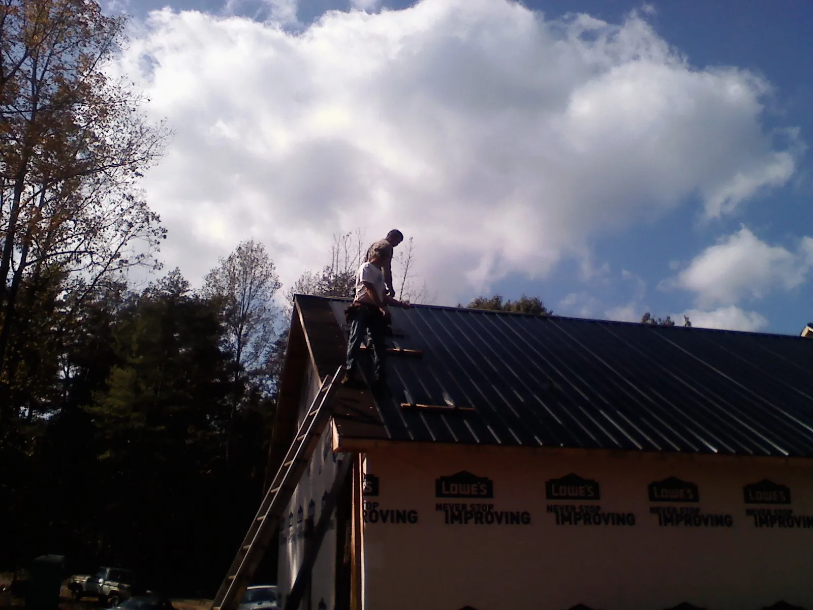 Roofer fastening dark metal panels high against a cloudy sky, from a Roof Inspection job in Hartleton