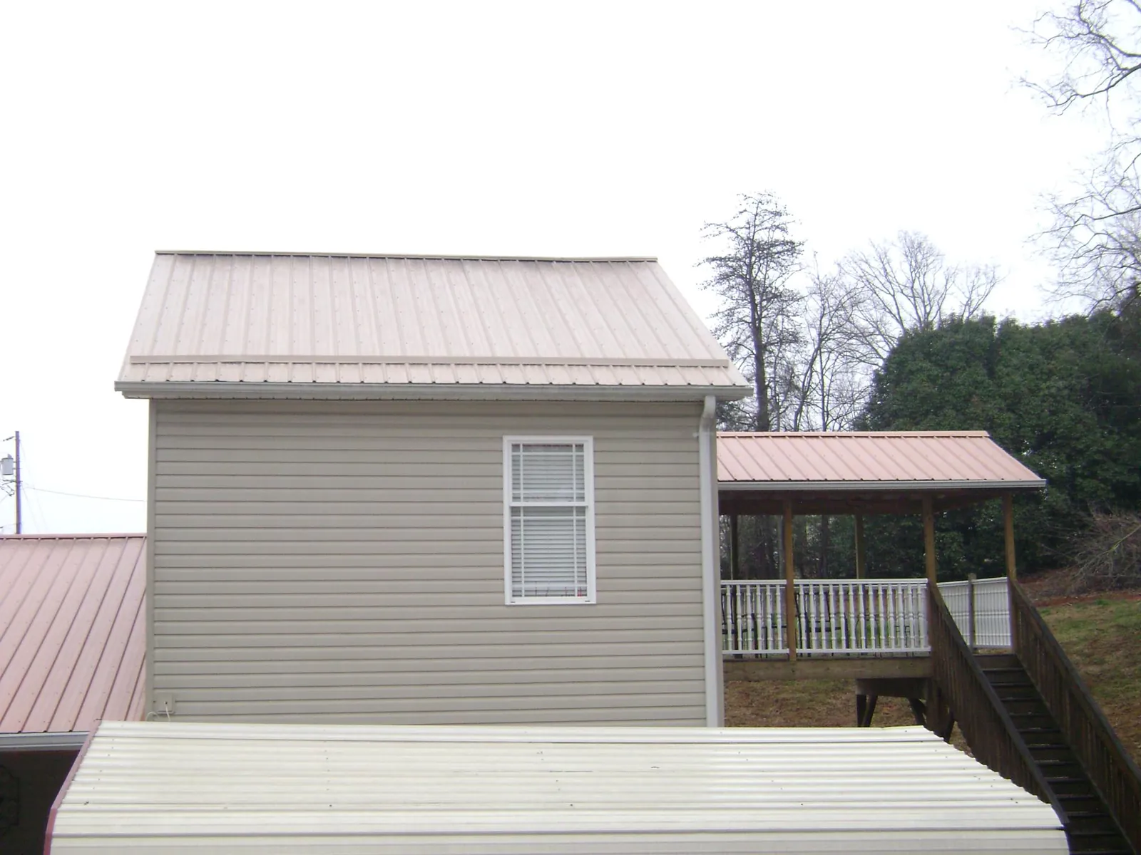 Tan metal roofs on a two story addition and attached porch, from a Roof Replacement job in Hartleton
